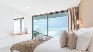 Ein modernes Schlafzimmer mit einem großen Bett, Meerblick und einem Balkon.