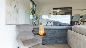 Un soggiorno moderno con una parete a parete in pietra, un'ampia finestra vista montagne e una poltrona contemporanea.
