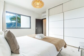 Ein modernes Schlafzimmer mit einem großen Bett, Blick ins Freie und einem Kleiderschrank.