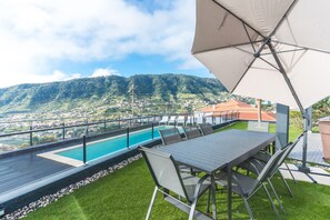 Eine Dachterrasse mit Pool, Esstisch und Stühlen mit Blick auf eine gebirgige Landschaft.