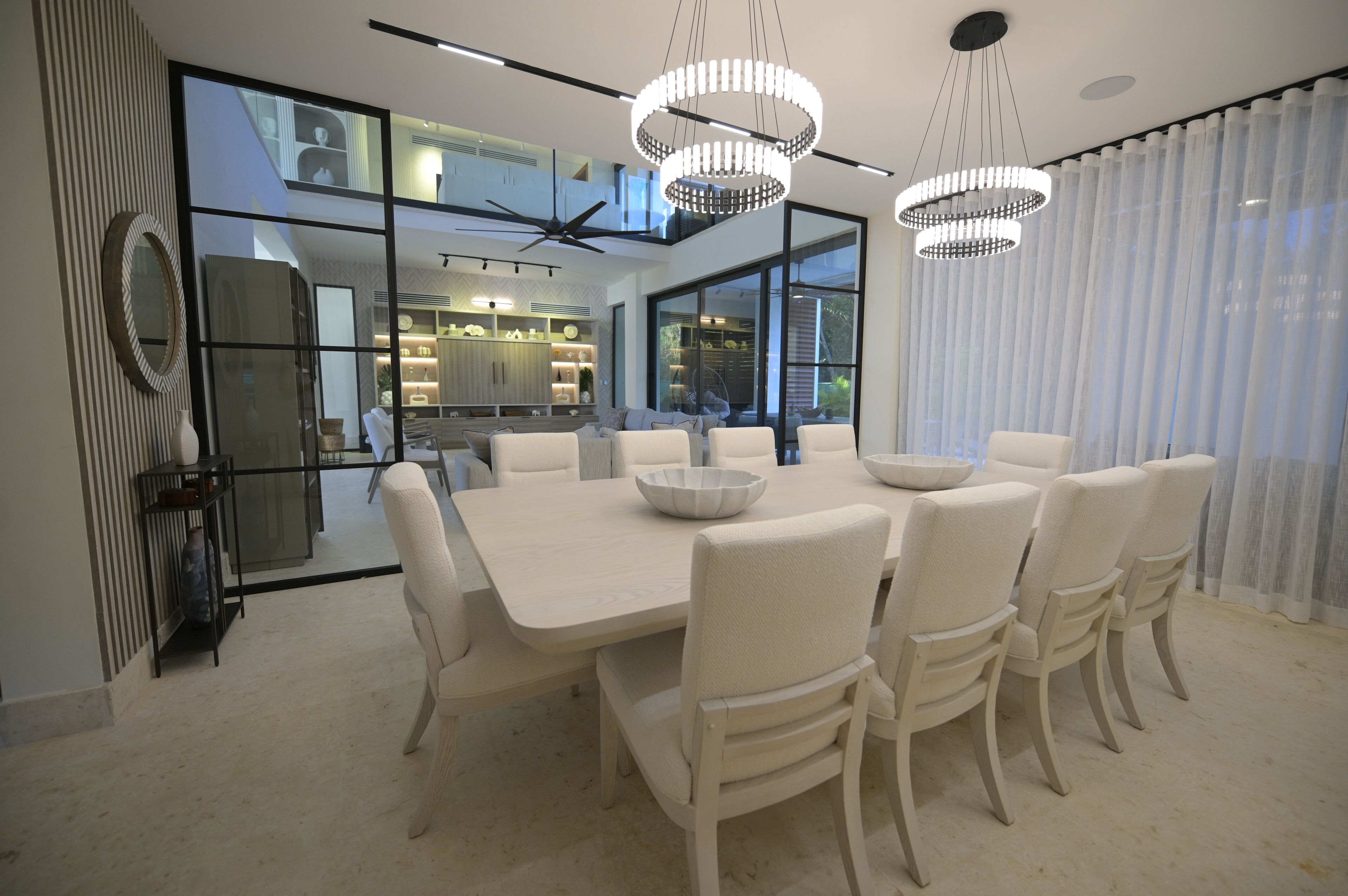 A modern dining area with a large table, white chairs, and pendant lighting.