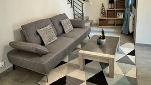 Ein modernes Wohnzimmer mit einem grauen Sofa, einem Holztisch und einem Teppich mit geometrischem Muster.