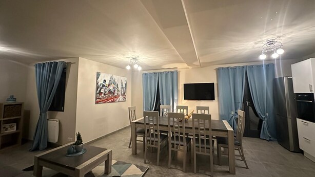 Ein modernes Wohnzimmer mit Essbereich, einem an der Wand befestigten Flachbildfernseher und einer Küche mit Kühlschrank und Backofen.