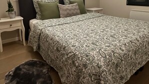 Ein Schlafzimmer mit einem Bett, zwei Nachttischen, einem Beistelltisch, einer Topfpflanze und einem Hundebett.