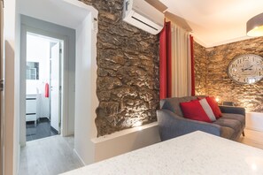 Ein modernes Wohnzimmer mit einer Wand aus Stein, einem grauen Sofa mit roten Kissen, einem weißen Couchtisch und einer Wanduhr.
