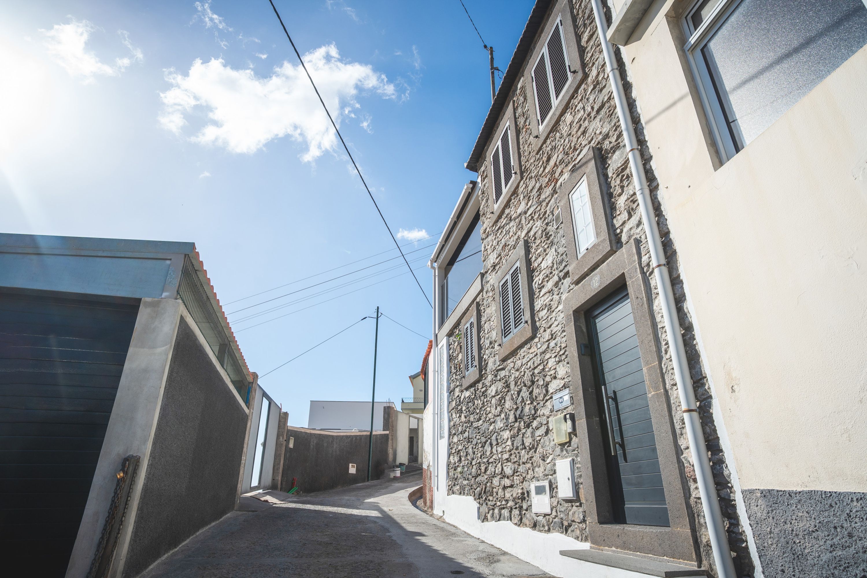 A narrow street with buildings on either side, featuring stone and plaster facades, and a clear sky above.