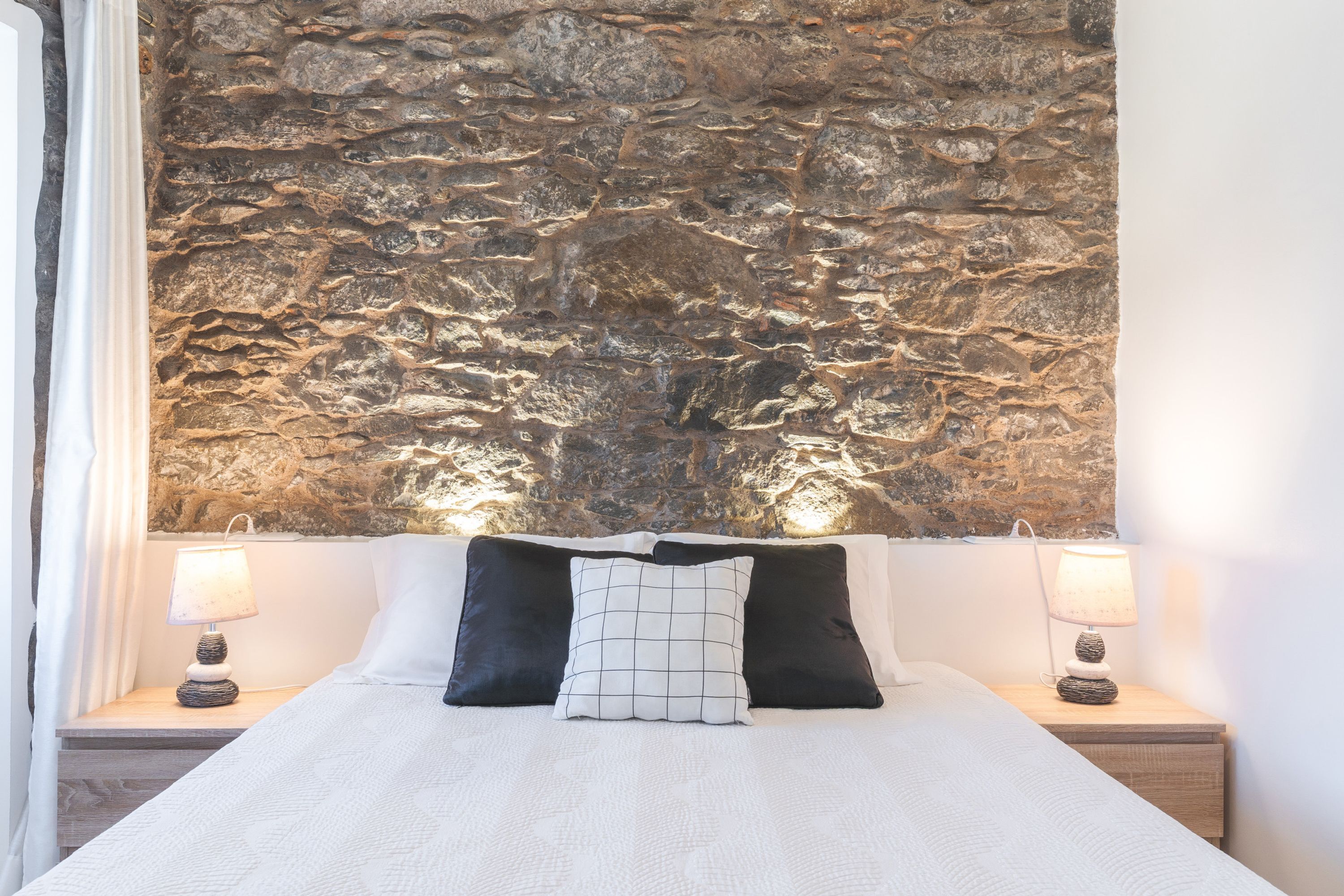 Ein Bett mit weißer Bettwäsche, zwei schwarze Kissen und eine strukturierte Wand im Hintergrund.