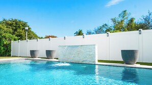 A swimming pool with a waterfall feature, surrounded by a white fence and large planters. - Modern Coastal Home in West Palm Beach with Pool (West Palm Beach)