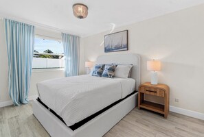 Un dormitorio con cama, dos lámparas de noche, una mesita de noche, una ventana con cortinas y un cuadro en la pared.