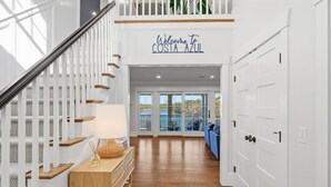 Una escalera con barandilla blanca, una mesa consola de madera con una lámpara y un cartel que dice 'Welcome to Costa Azul'.