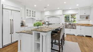 Una cocina moderna con armarios blancos, encimera de granito y una isla central con taburetes de bar.