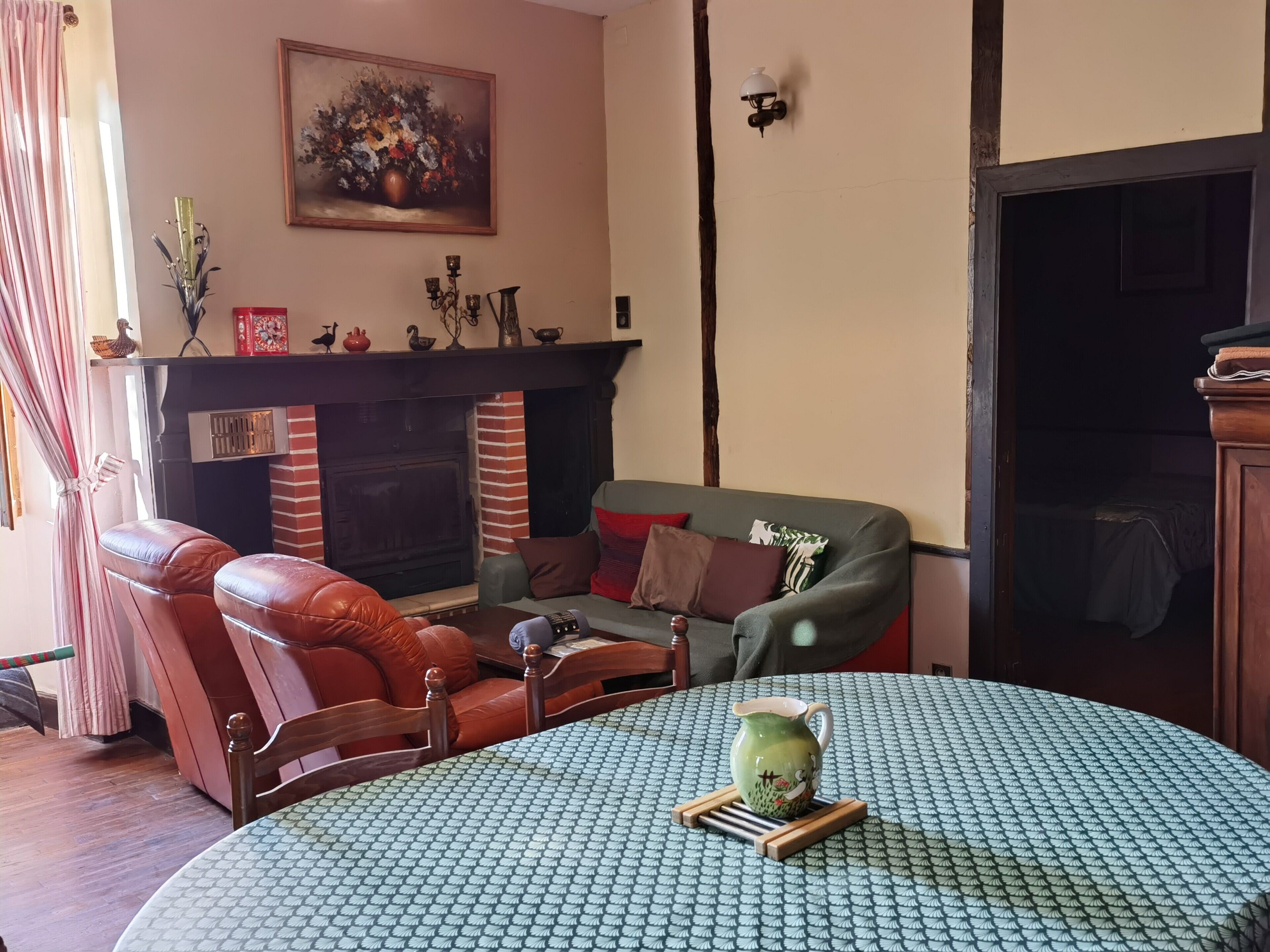 Una sala de estar con chimenea, sillón de cuero, sofá y una mesa redonda con mantel estampado.