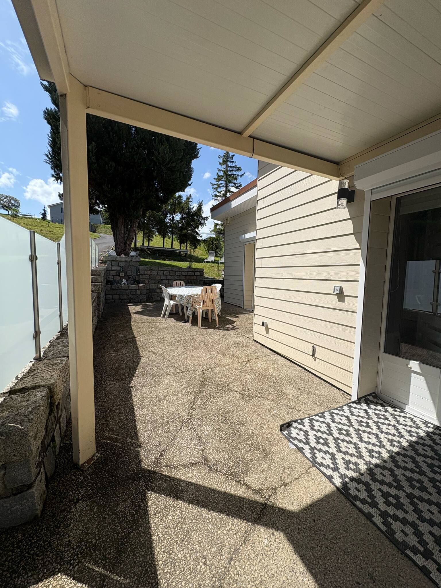 Un patio al aire libre con zona de estar techada, un muro de piedra y vistas a un barrio residencial.