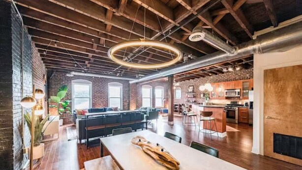 Ein geräumiges Loft mit freiliegenden Ziegelwänden, einem großzügigen Essbereich und einer Küche mit Barhocker.