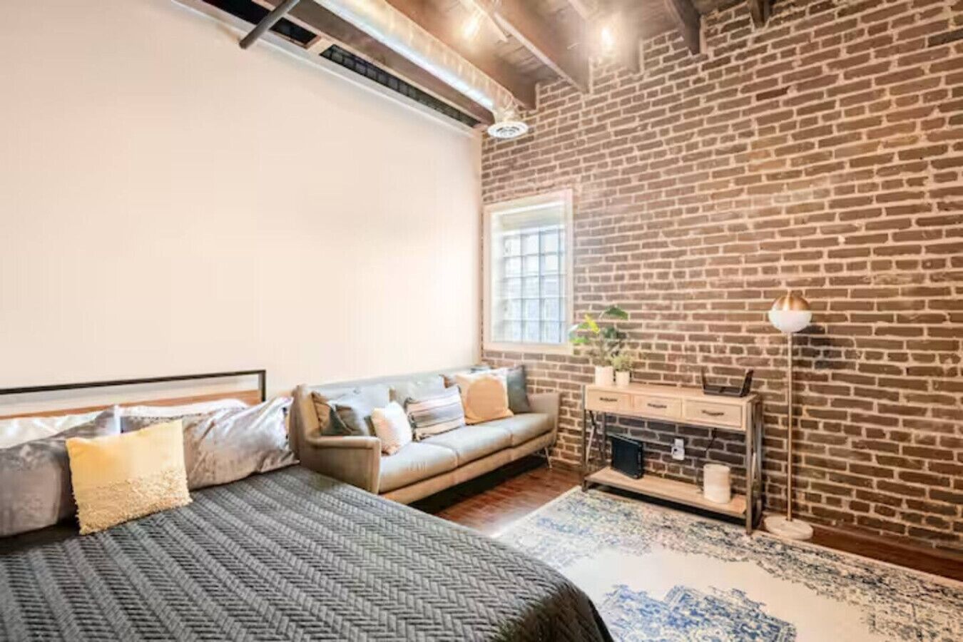 A bedroom with a brick wall, a sofa, a bed, and a nightstand.