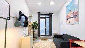 Una sala de estar moderna con un sofá, una mesita, una lámpara, un televisor y una ventana con cortinas.