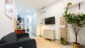 Una sala de estar moderna con un sofá, un televisor montado en la pared, un mueble, una planta y un pequeño estante de madera.