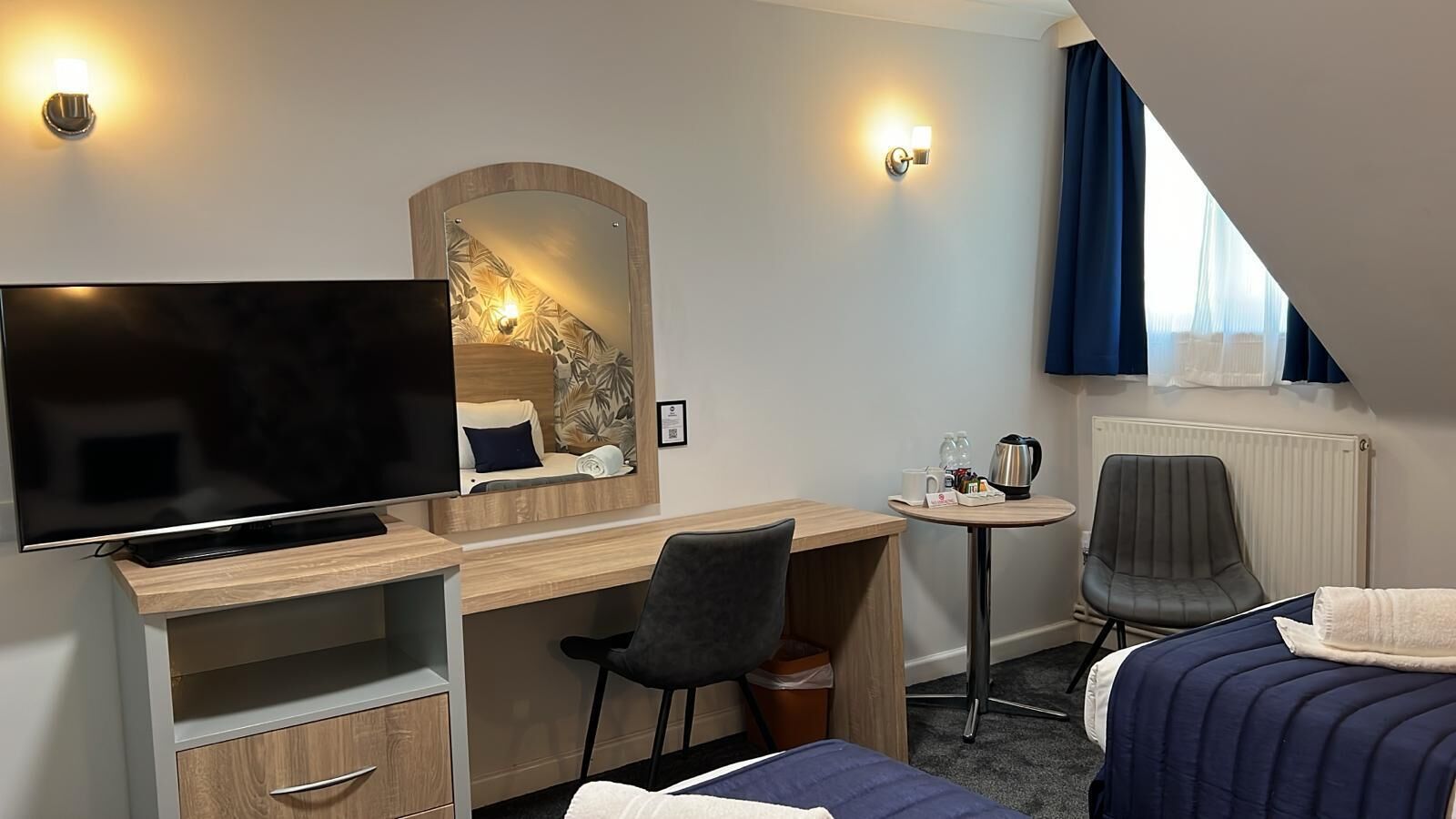 Een hotelkamer met een televisie, een bureau, een stoel, een klein tafeltje met een waterkoker en een bed.