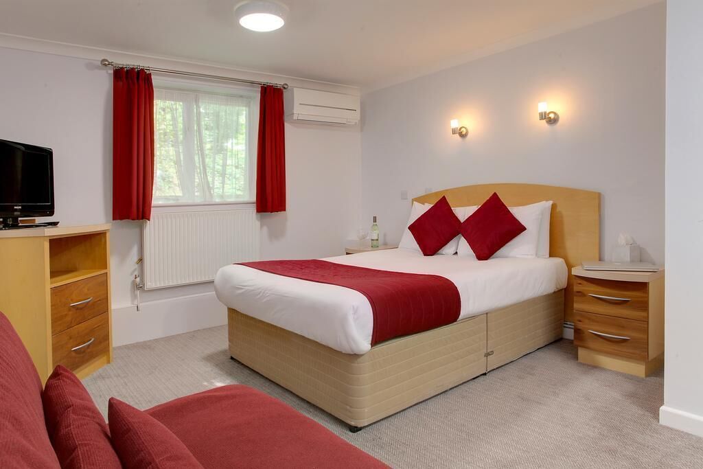 A hotel room with a bed, bedside tables, a TV, and a window with curtains.