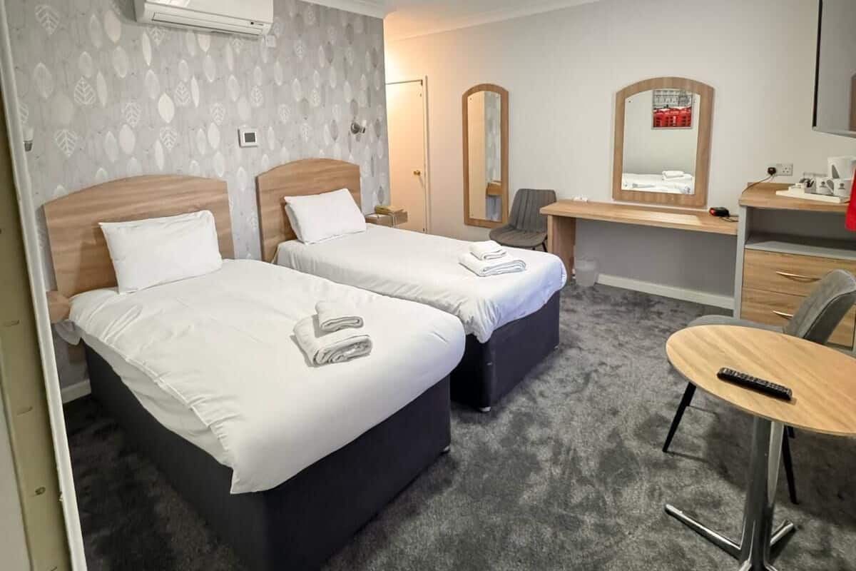 A hotel room with two beds, a desk, a chair, and a small table.