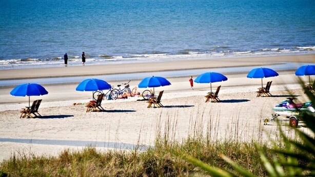 Una playa con varias sombrillas azules y sillas de playa.