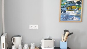 Et køkken med et træskab, kaffemaskine, brødrister og et billede i ramme på væggen.