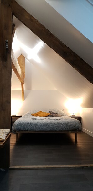 A bedroom with a sloped ceiling, a bed with a patterned bedspread, and two bedside lamps. - Cozy, quiet apartment in the heart of Intra-Muros!   (Saint-Malo)