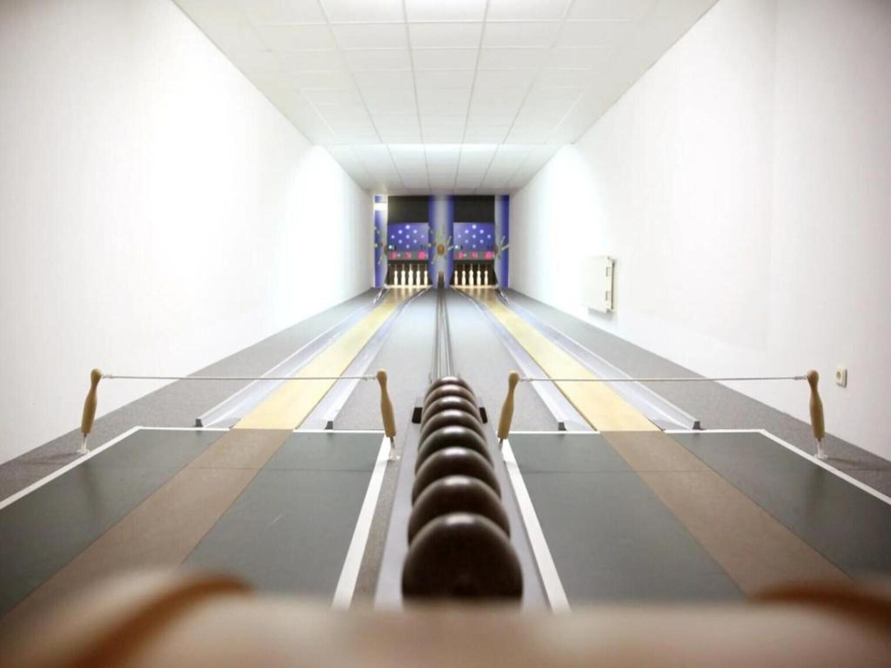 A bowling alley with lanes, pins, and a bowling ball in the foreground.