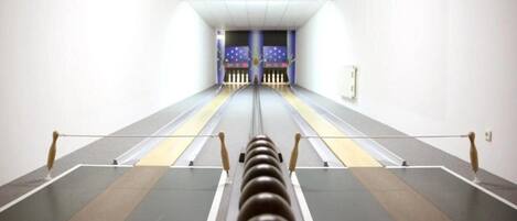 A bowling alley with lanes, pins, and a bowling ball in the foreground.