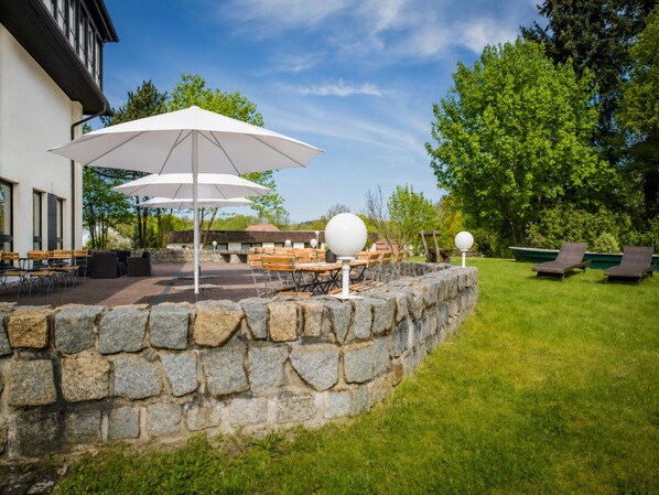 An outdoor patio with stone walls, tables, chairs, and umbrellas.