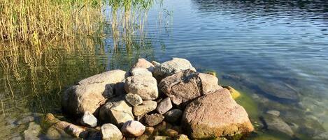 A calm lake with clear water, surrounded by rocks and reeds.