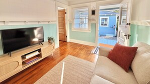 A living room with a flat-screen TV, wooden entertainment unit, and a beige sofa with a red pillow.