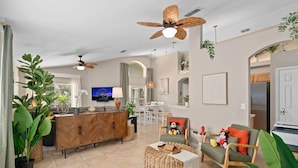 Ein modernes Wohnzimmer mit einem Holzkasten, einem Fernseher, einem Deckenventilator und einem Essbereich im Hintergrund.