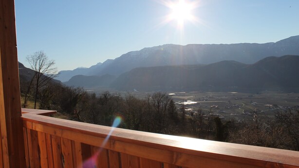Een houten balkon met uitzicht op een bergachtig landschap onder een heldere lucht.