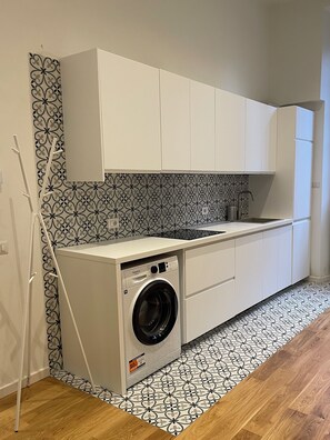 A compact kitchen with a built-in washer and dryer, white cabinets, patterned backsplash, and a wooden floor. - Russo 15 - Modern one-bedroom apartment in central Milan neighborhood (Milano)