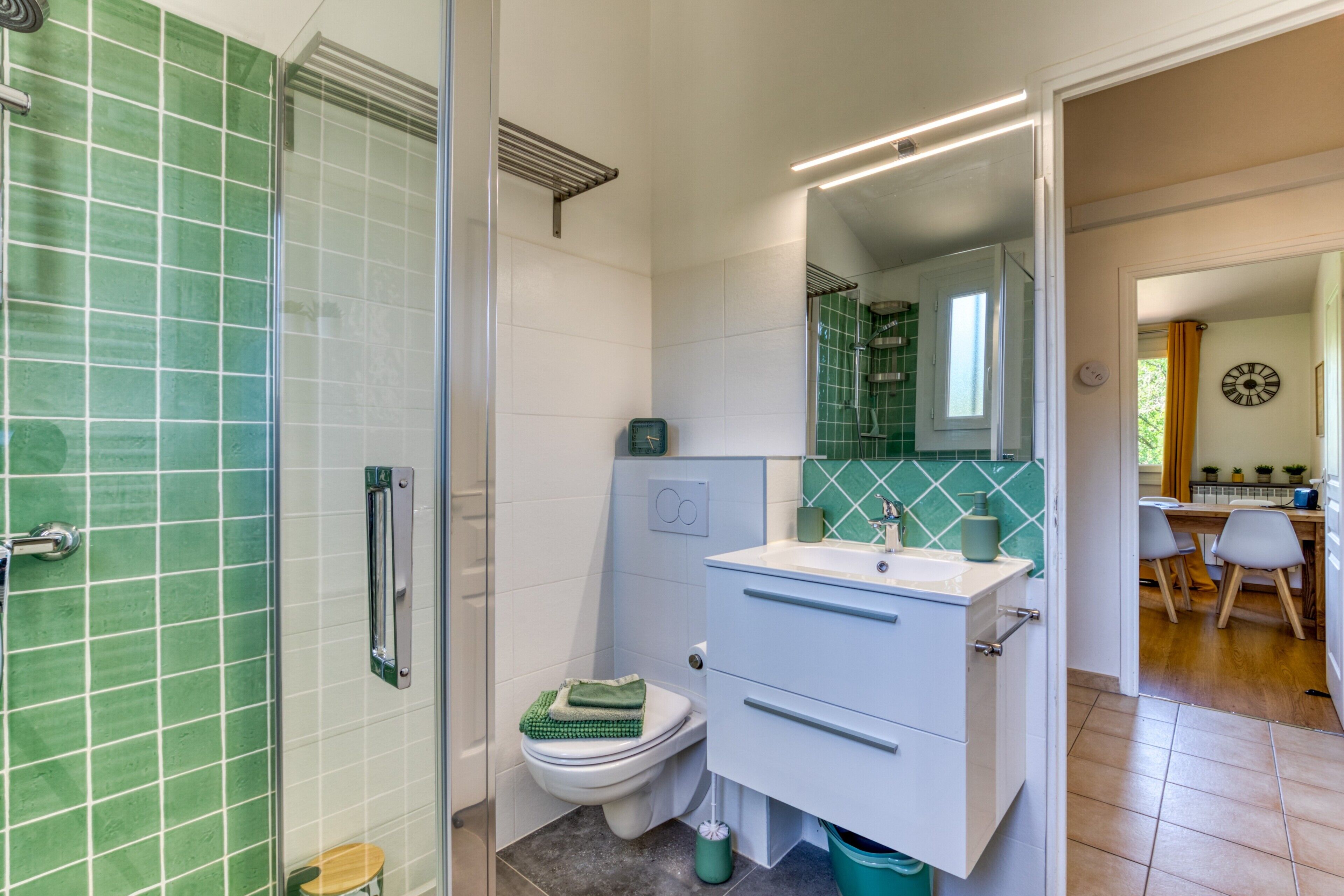 A bathroom with a shower, toilet, and sink, with green tiles and a mirror above the sink.