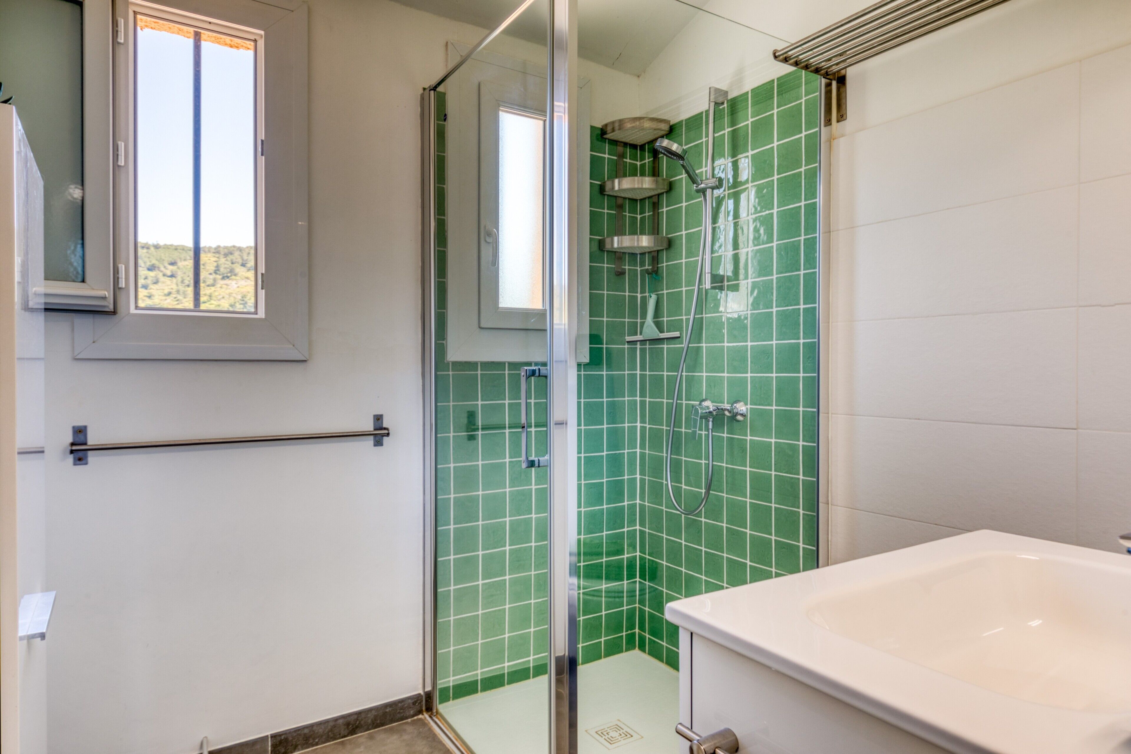 A bathroom with a glass-enclosed shower, a white bathtub, and green tiled walls.