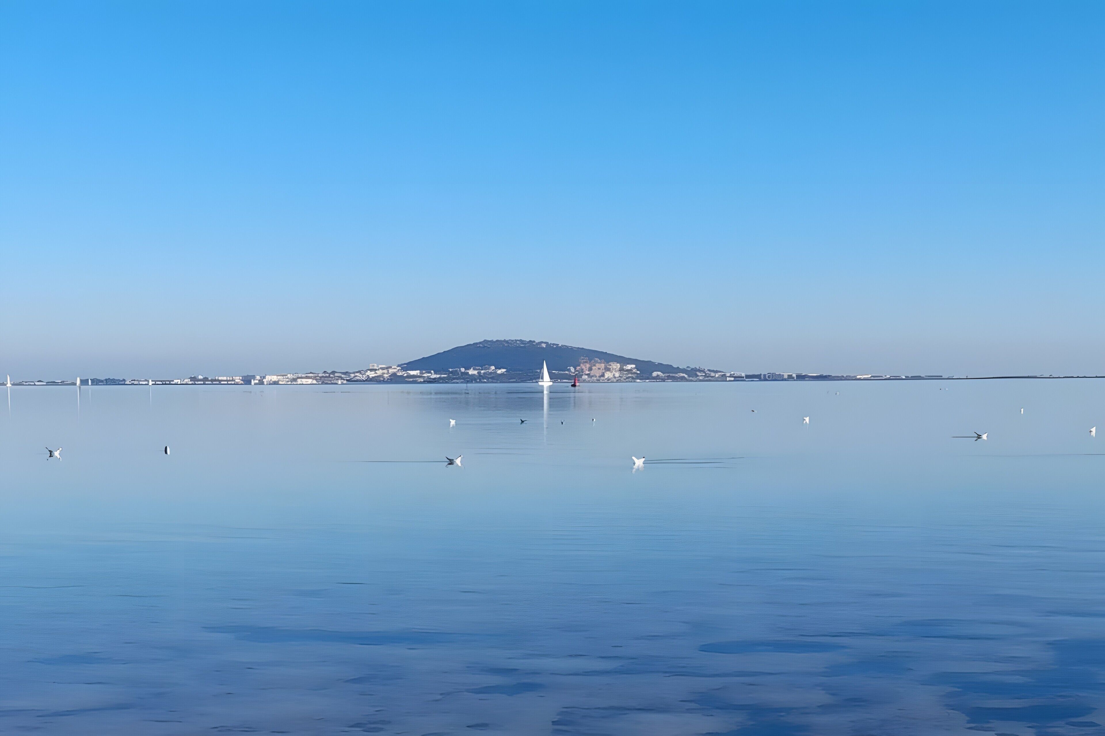 Un plan d’eau calme, avec une montagne lointaine et un voilier.