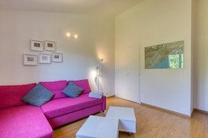 Una sala de estar moderna con un sofá rosa, una mesa de centro blanca, una lámpara de pie y un cuadro abstracto grande en la pared.
