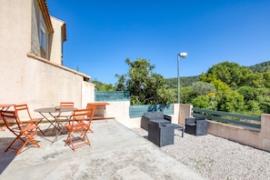 Un patio exterior con una mesa, sillas, una lámpara y vistas a una colina.