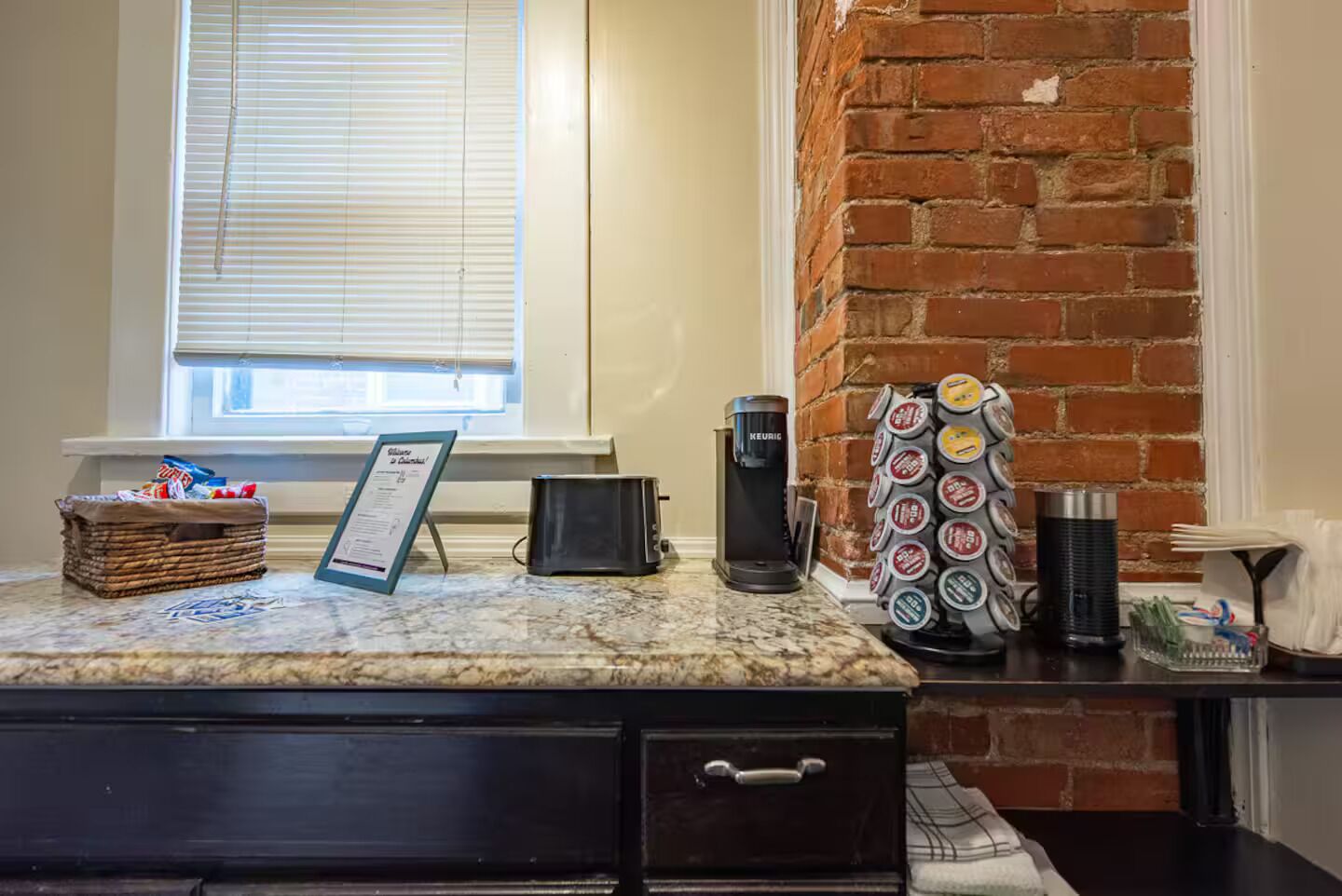 A kitchen counter with a coffee maker, a basket of snacks, and a coffee pod holder.