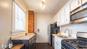 A compact kitchen with a brick accent wall, stainless steel appliances, and a wooden bar area. - 3-Bedroom in Downtown Columbus (Columbus)