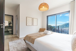 A modern hotel room with a large bed, a view of the city and mountains, a balcony with a chair, and a large window. - Villa Sofia by Atlantic Holiday (Machico)