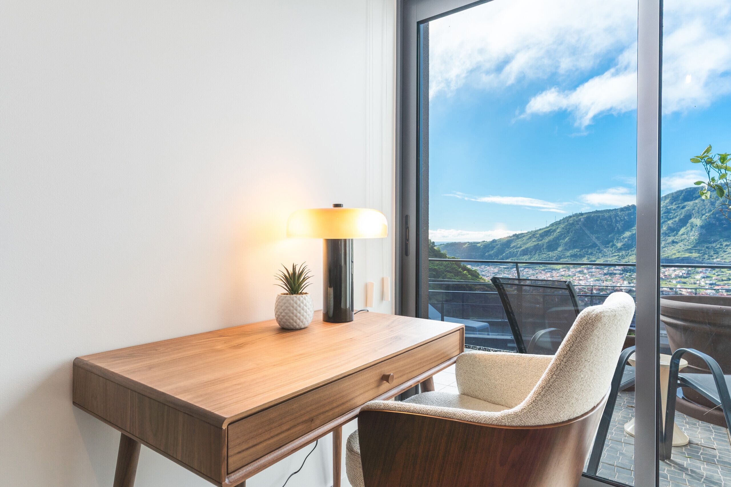 A modern room with a wooden desk, a lamp, a potted plant, and a chair.