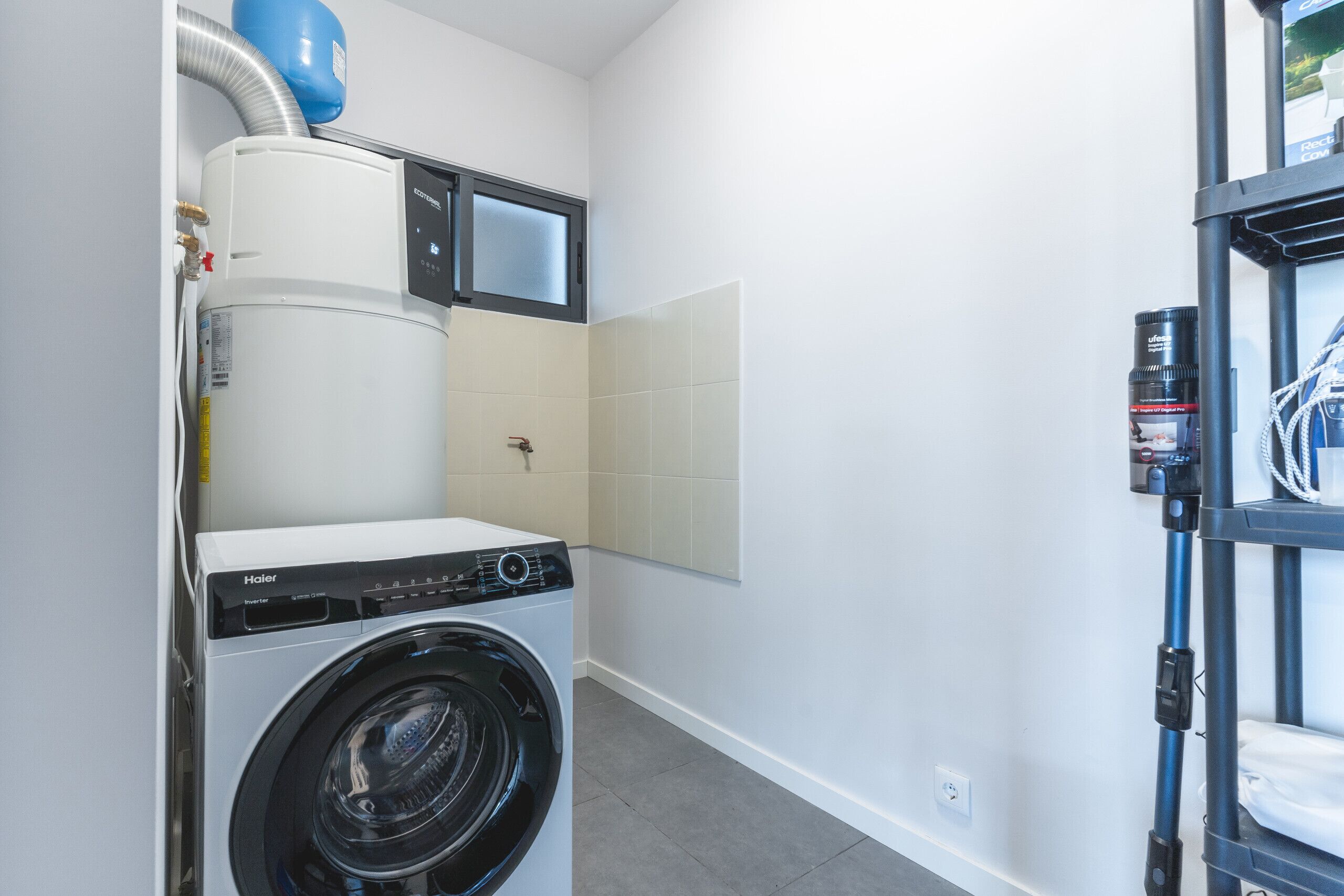 A compact laundry area with a front-loading washer and dryer, a water heater, and a small window.