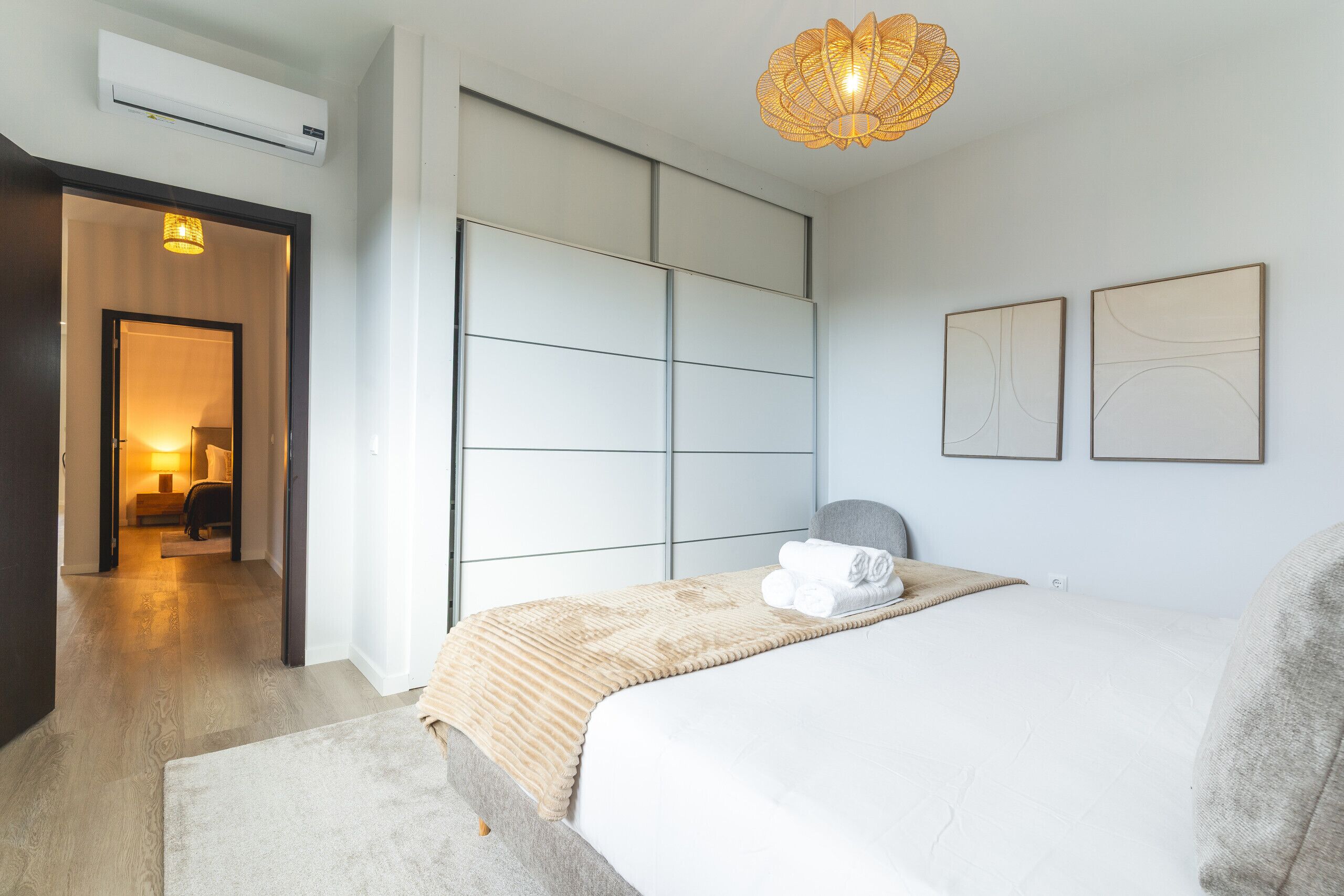Camera da letto moderna con un letto grande, un armadio a muro e un corridoio che porta a un soggiorno.