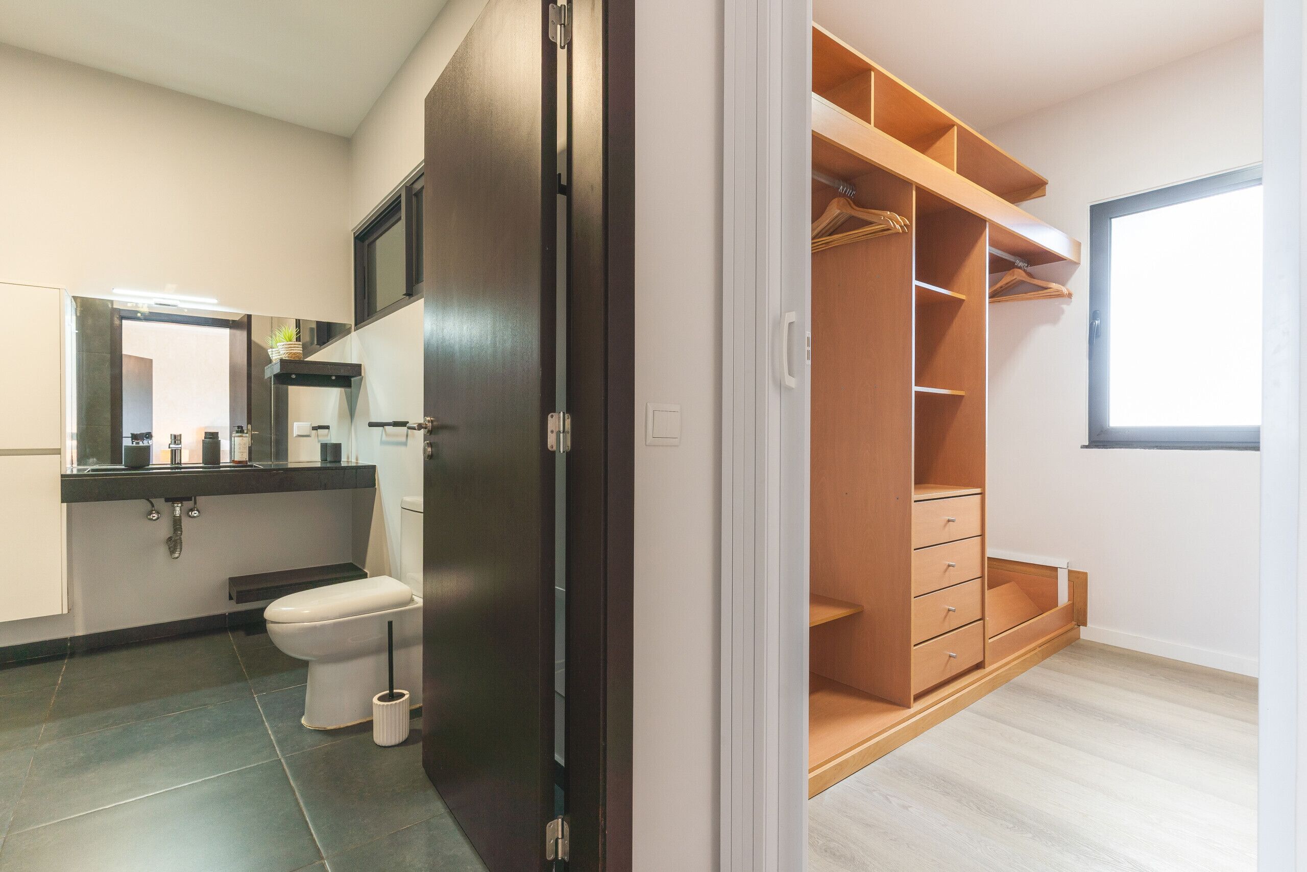Ein modernes Badezimmer mit Toilette, Waschbecken und Spiegel. Ein Holzkasten mit mehreren Regalen und Schubladen steht ebenfalls bereit.