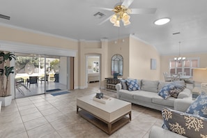 A spacious living room with a large sofa, a coffee table, and a ceiling fan. There is a sliding glass door leading to an outdoor patio area. - 3/2 Designer in the Village of Piedmont (The Villages)