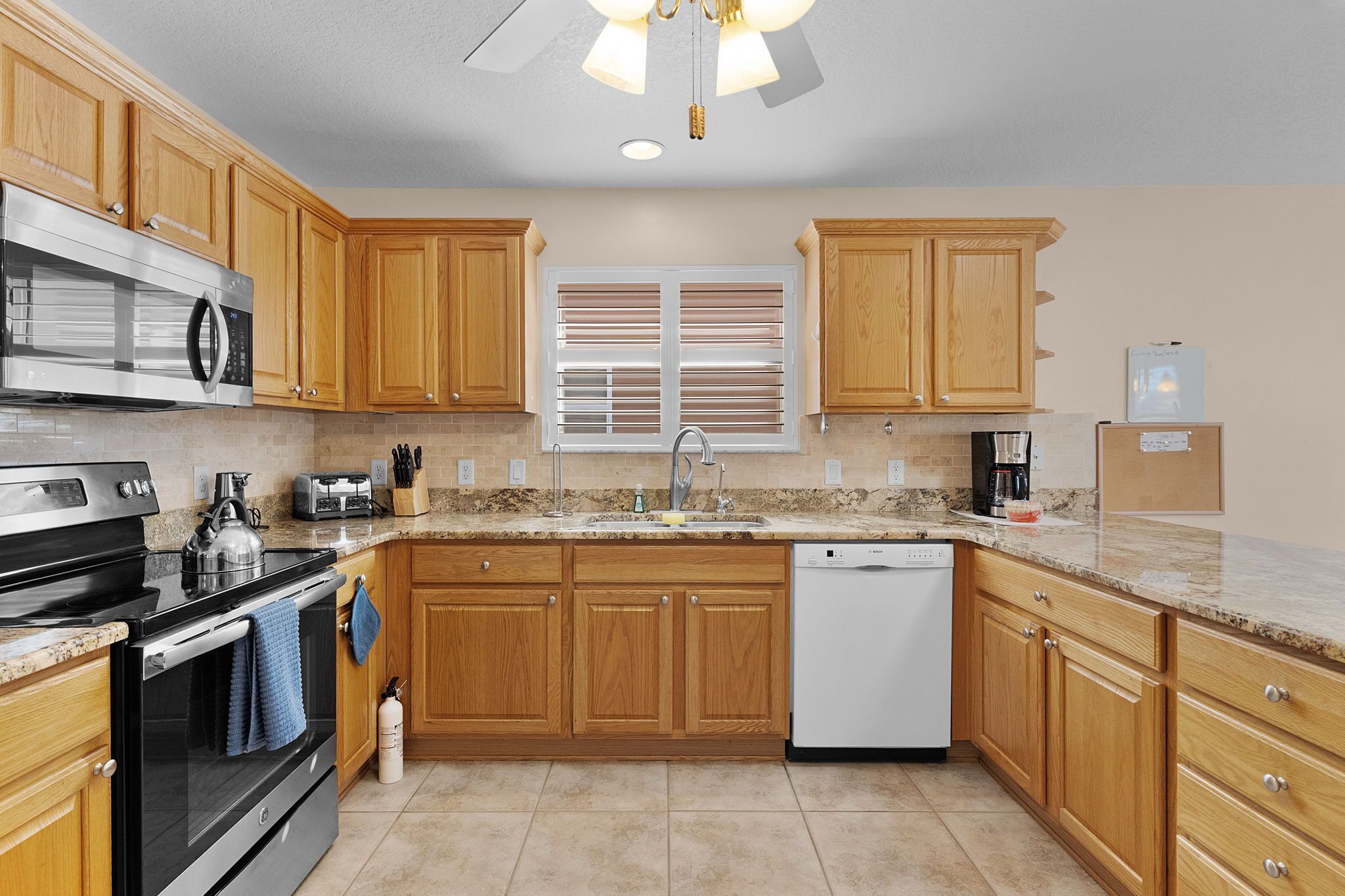 A kitchen with wooden cabinets, a stainless steel stove, a dishwasher, and a window with blinds.