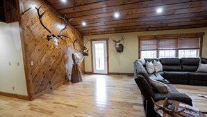 Un salón amplio con pisos de madera, un sofá de cuero tipo seccional y cornamentas de ciervo colgadas en la pared.